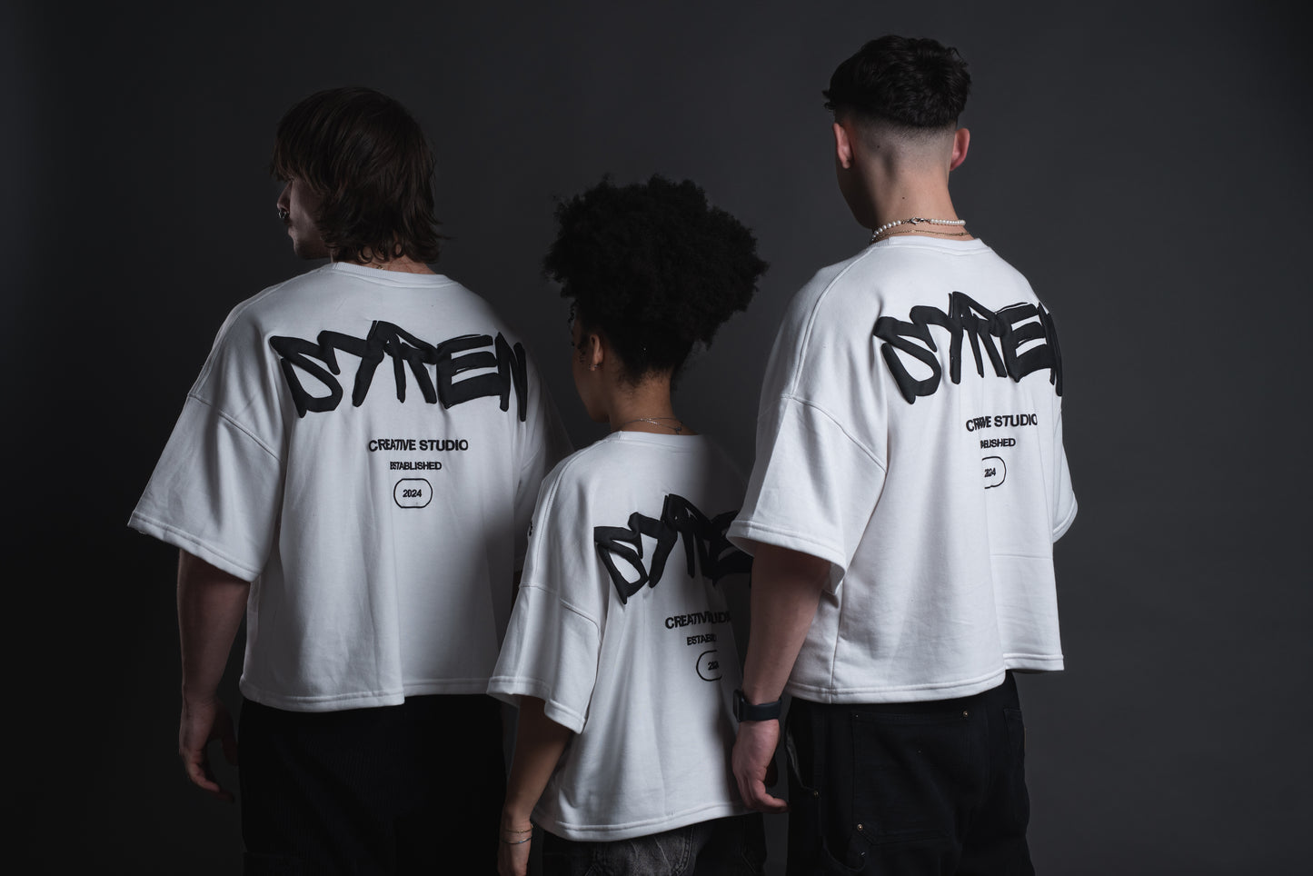 Back view of three models in SYREN 1.0 oversized tees showing bold logo.